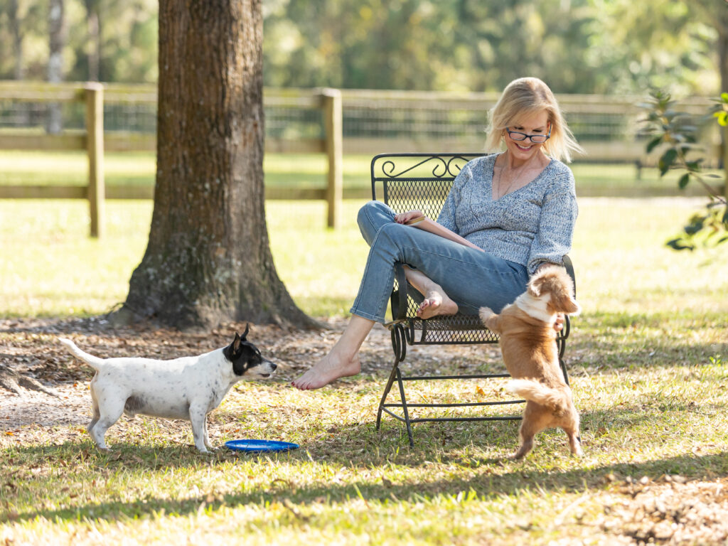 Woman sittig on a gaden chair in her yard with her pet dogs